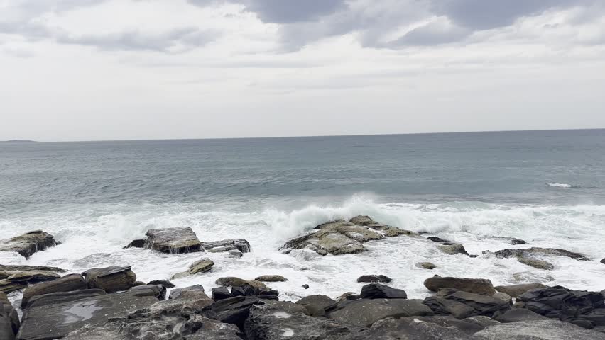 Rough ocean waves crashing against rocky shore on a cloudy day