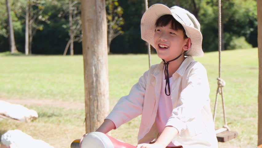 Happy boy in a safari hat plays on a red scooter statue in the park