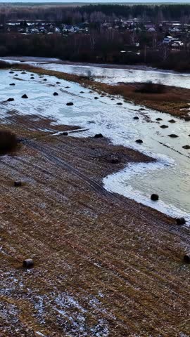 Snow covered rural fields with scattered hay bales near village, drone aerial vertical of frozen farmland
