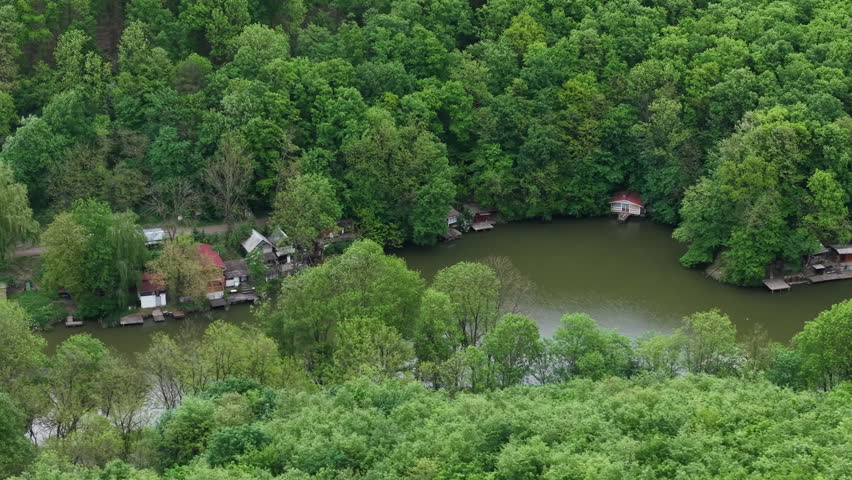 A high angle view captures small wooden houses and cabins situated along the edge of a calm lake in dense forest.