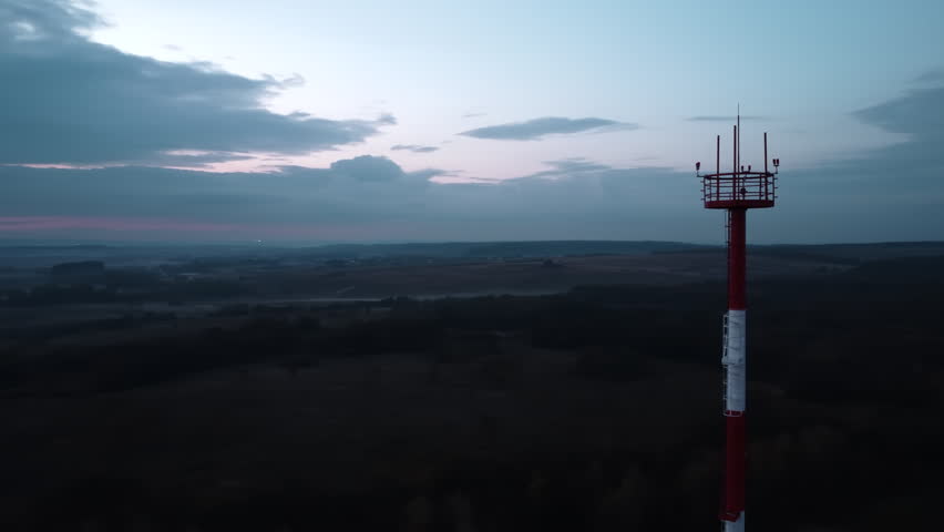 Red and white communications tower above rural landscape at dawn
