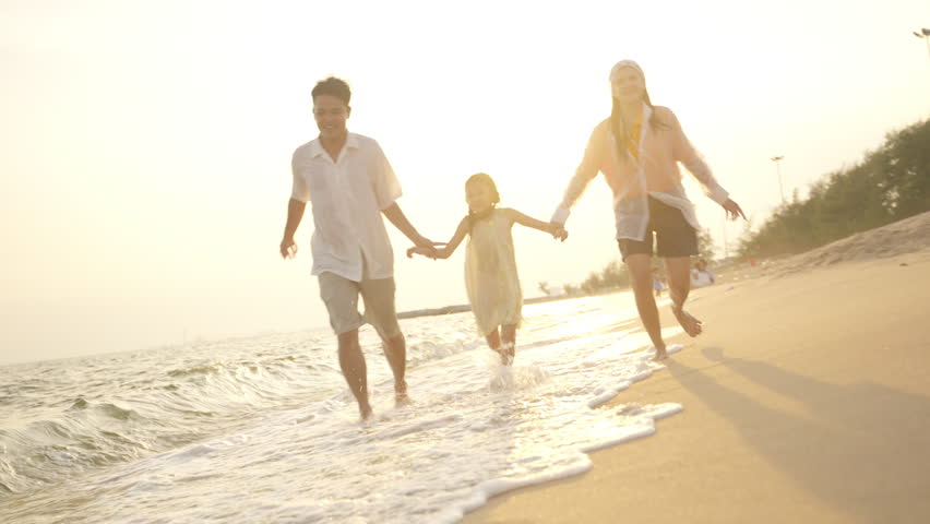Happy Asian family parents and child running and playing together at tropical beach. Father, mother and little daughter enjoy outdoor active lifestyle travel the ocean on summer holiday vacation. Family bonding and childhood memories.
