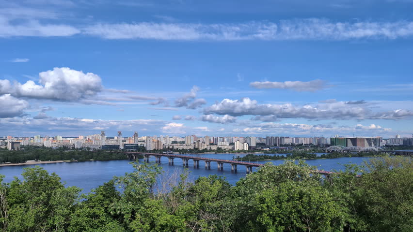 Panoramic scenic view of Kyiv left bank residential districts across the Dnieper river with Paton bridge under a blue sky with fluffy white clouds