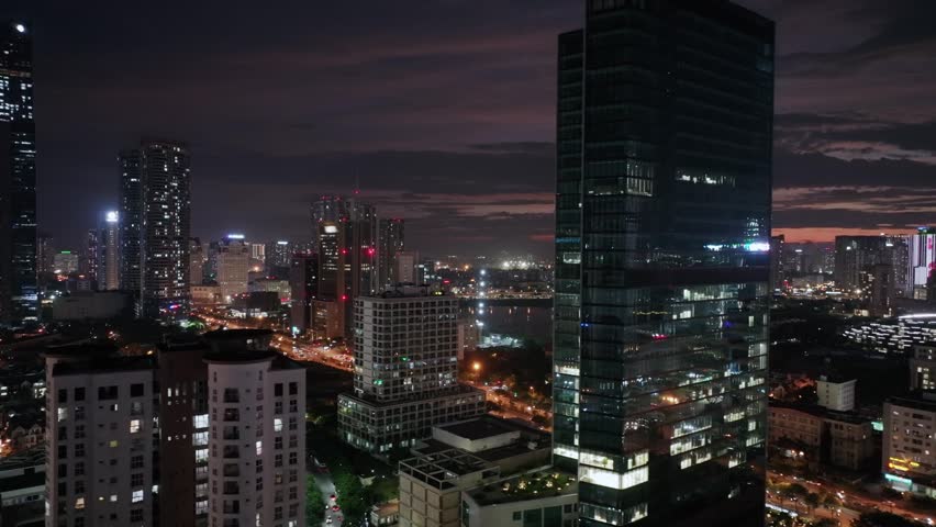 Night cityscape near Cau Giay Lake in Hanoi featuring illuminated office towers, busy streets, and modern urban architecture.