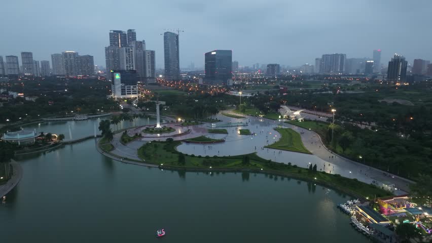 Dusk view of the central monument plaza in Hoa Binh Park surrounded by gardens, pathways, and modern city buildings.