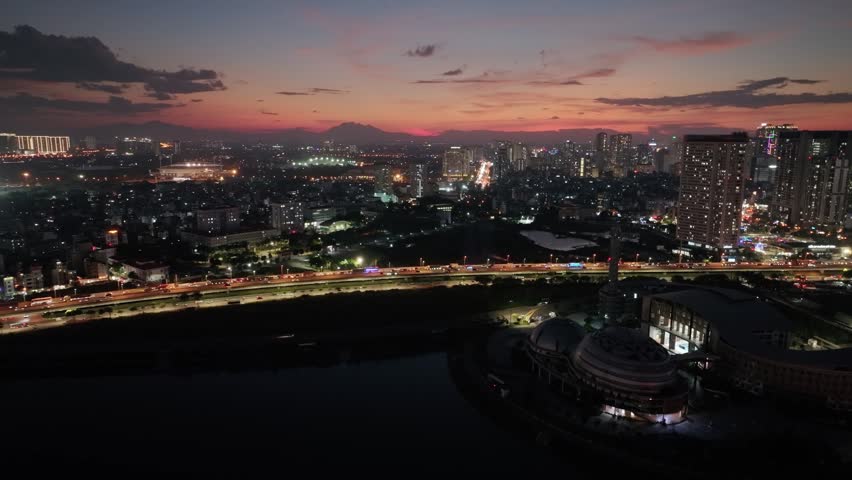 Aerial sunset view of Pham Hung Street in Hanoi with illuminated traffic corridors, urban neighborhoods, and a vibrant city skyline.