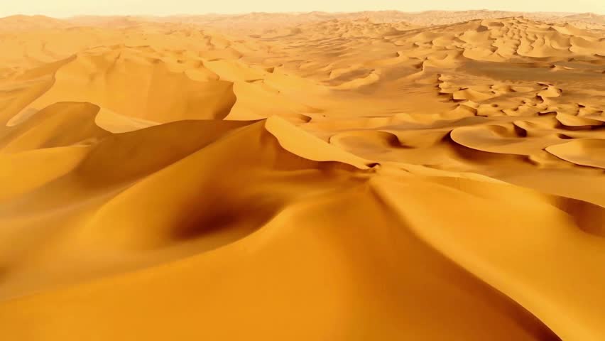 An aerial view of vast, rolling sand dunes at sunset