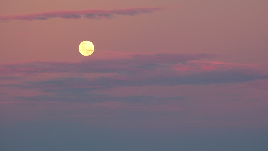 Ominous yellow full moon rising in vivid twilight sky with some wispy clouds