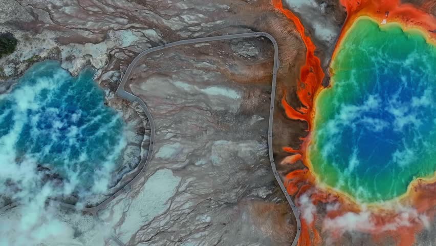Boardwalk walk way trail Midway Geyser Basin two vibrant turquoise hot springs pool Grand Prismatic Spring birdseye aerial drone Yellowstone National Park Wyoming volcanic thermal hot steam upwards