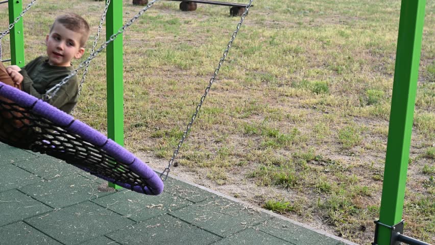A boy riding on a round net swing in a garden