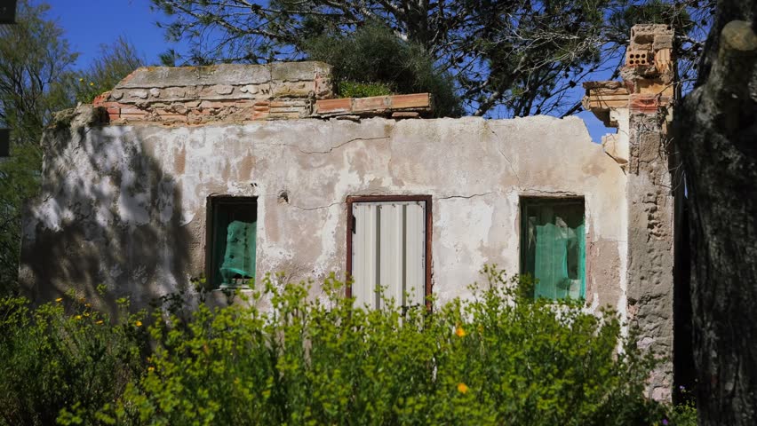 Abandoned old house surrounded by trees in a rural landscape under blue sky. Concept of depopulation, migration, urban decay and deserted villages. High quality 4k footage