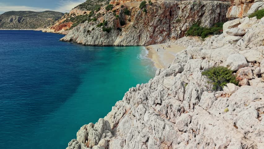 Turquoise Mediterranean sea washes pristine sand of Kaputas Beach, Turkey. Majestic steep rocky cliffs enclose hidden coastal bay in Turkish Riviera. 4K aerial of sunny Antalya shoreline