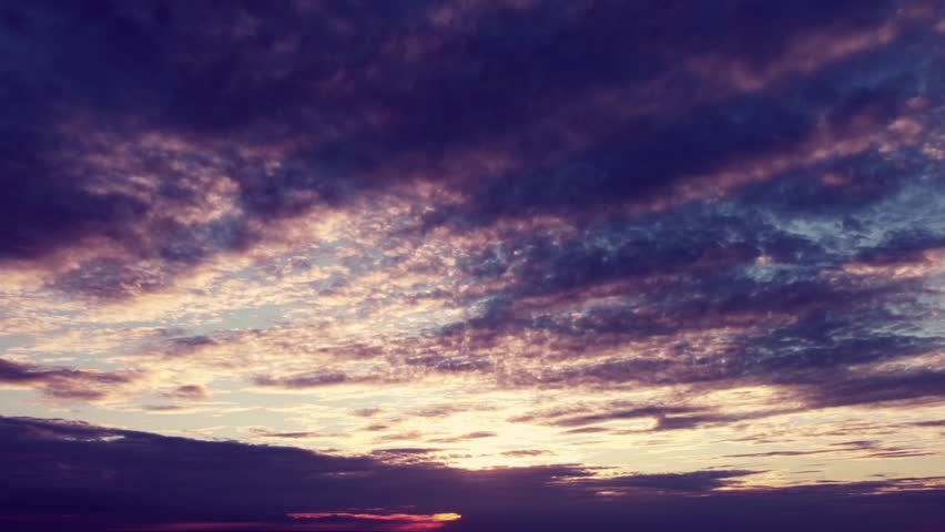A stunning time-lapse capturing the beauty of the sky at dusk. A dramatic blend of deep purples blankets the clouds, while the golden glow of the setting sun radiates warmth from beyond the horizon.