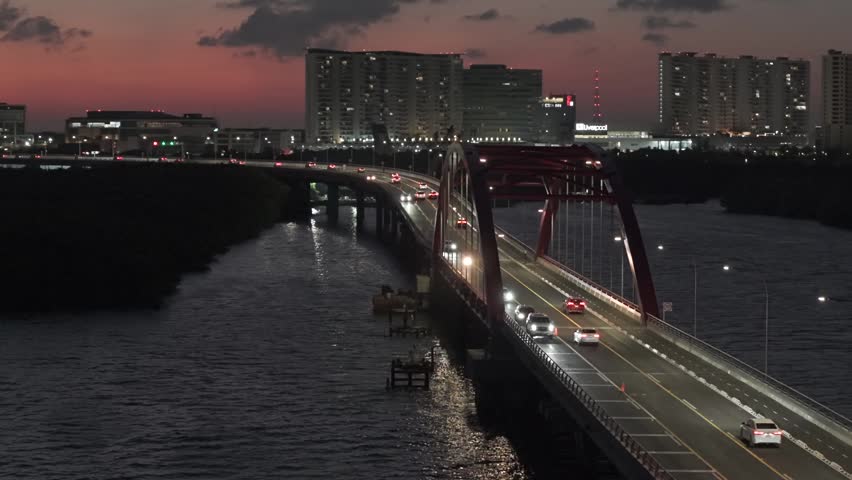 Night aerial drone view of the Nichupté Bridge illuminated over the lagoon in Cancún, Mexico, with the sparkling lights of downtown creating a stunning urban skyline.