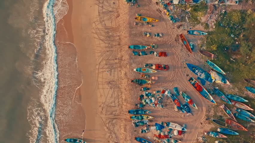 Aerial shot of vibrant boats lined along a sandy beach with ocean waves
