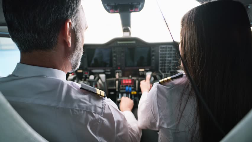 Male captain and female first officer preparing for takeoff in a modern aircraft cockpit. The senior pilot instructs the trainee on the flight deck