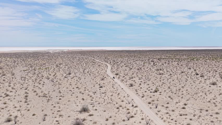 SUV pulls a teardrop camper trailer across Baja desert near El Salar salt flats in California. Clear skies and open land surround them.