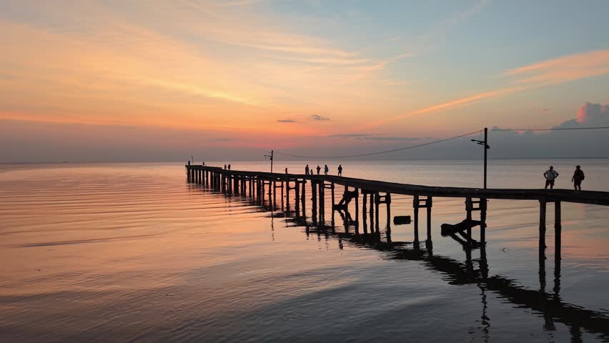 People walking on a wooden pier at Segenting beach during a pastel colored sunset.