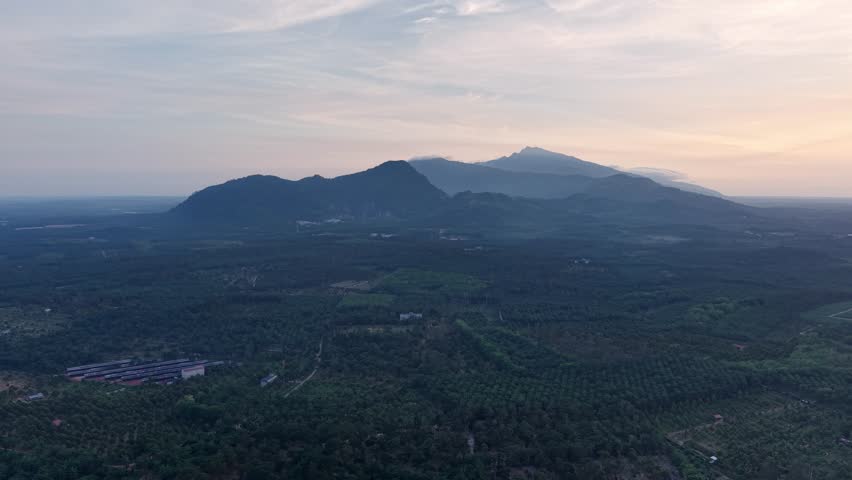 Sunset aerial view over Tangkak palm plantations, rolling hills and distant mountains.