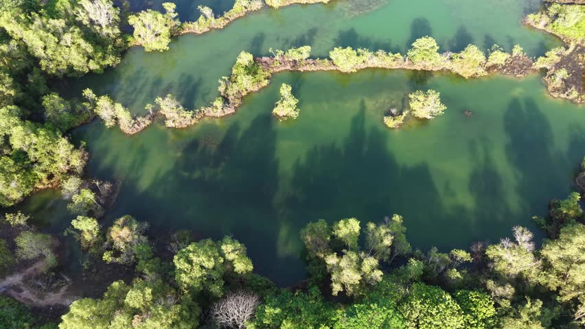 Top down aerial footage of an abandoned quarry lake surrounded by trees and small islands.