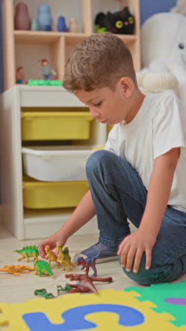 Boy kneeling and playing with plastic dinosaur toys, hand placing figures on foam playmat in building; concentration imagination.