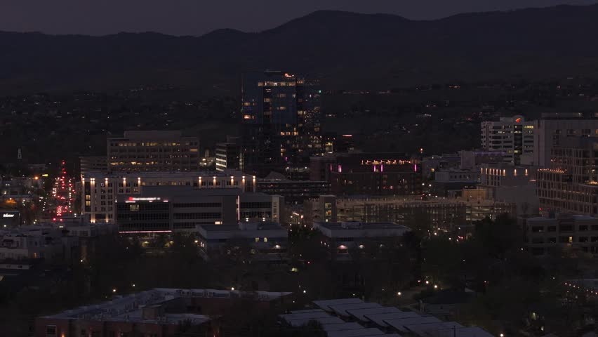 Atmospheric nighttime slow panning drone shot of vibrant downtown Boise, Idaho. The city skyline sparkles with beautiful lights while vehicle traffic flows steadily along 13th and 11th streets. The iconic Arthur building is visible. Smooth panoramic movement reveals the glowing buildings, bridges, and urban energy reflected on the river. Perfect for city nightlife, urban lifestyle, travel, and cinematic night footage.