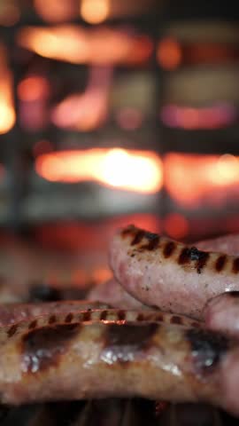 Delicious pork sausages sizzling on a hot barbecue grill. Flames and glowing embers create a warm, inviting background for this classic meal