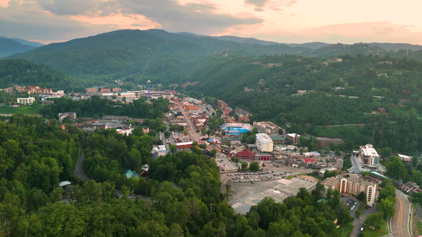 Aerial landscape of Gatlinburg city center at dusk with illuminated busy tourist streets and Smoky Mountains scenery.