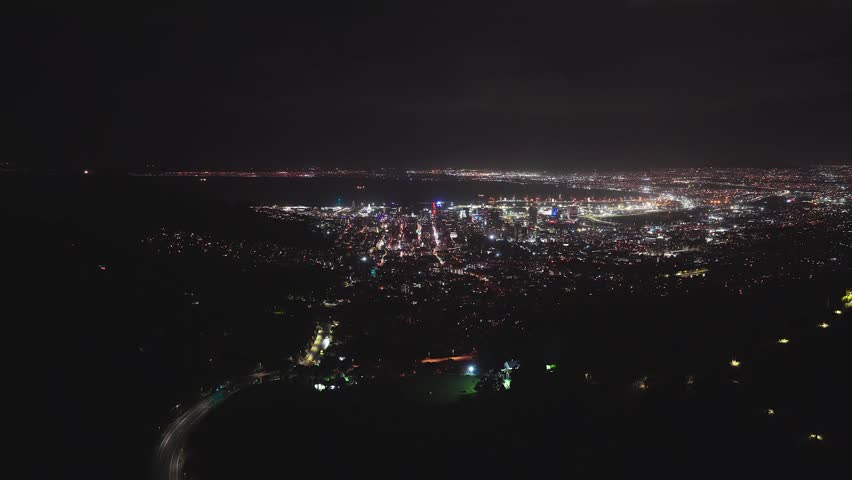 Aerial night view of Cape Town, South Africa, from mountain slopes shows downtown, V and A Waterfront, Table Bay, Cape Town Stadium, traffic flows, and low clouds.