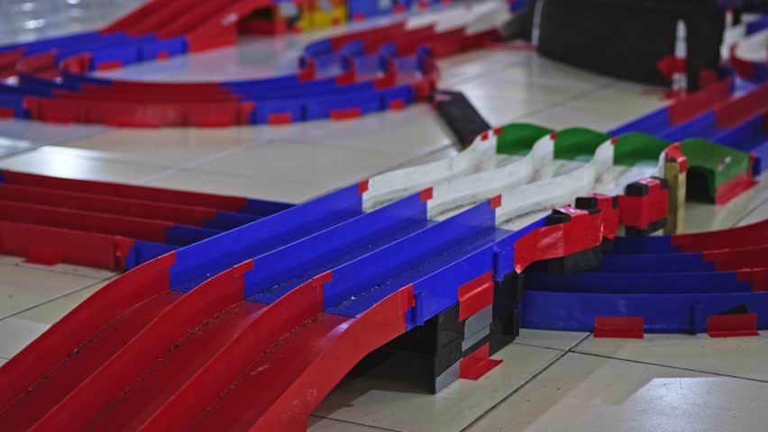 Three fast mini 4WD toy cars racing through a sharp turn on a colorful red, blue, and white plastic modular track layout.
