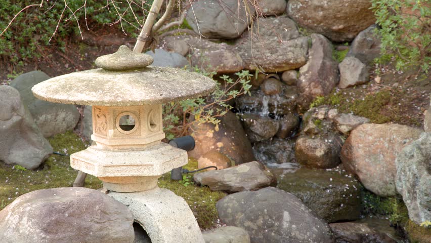 Static shot of a stone toro lantern near a flowing waterfall in Kanazawa, Japan