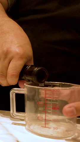 Close-up shot of hands pouring sake into a measuring cup and elegant wine glasses