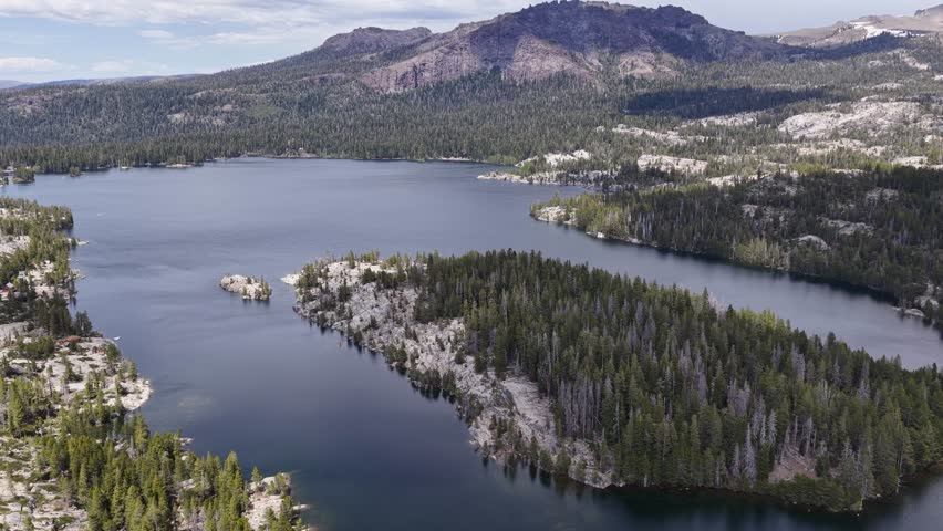 Aerial drone footage flying over Silver Lake, revealing its deep blue waters surrounded by a vast pine forest and granite mountains in the Sierra Nevada range near Pioneer, California