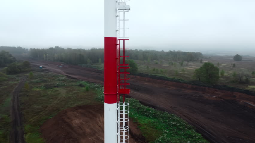Red and white metal tower above a foggy rural landscape