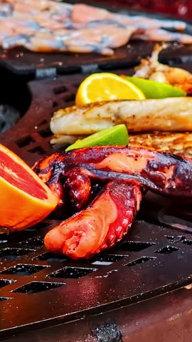 Assorted fresh seafood, octopus, and frog legs cooking on a hot barbecue grill outdoors