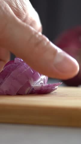 Hands cut red onion on wooden cutting board on background of vegetables and greens in kitchen. Choping. Cooking food. Vertical shot