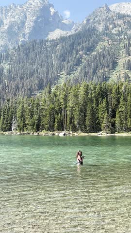 Woman swimming in String Lake with Grand Teton mountains on a summer day.