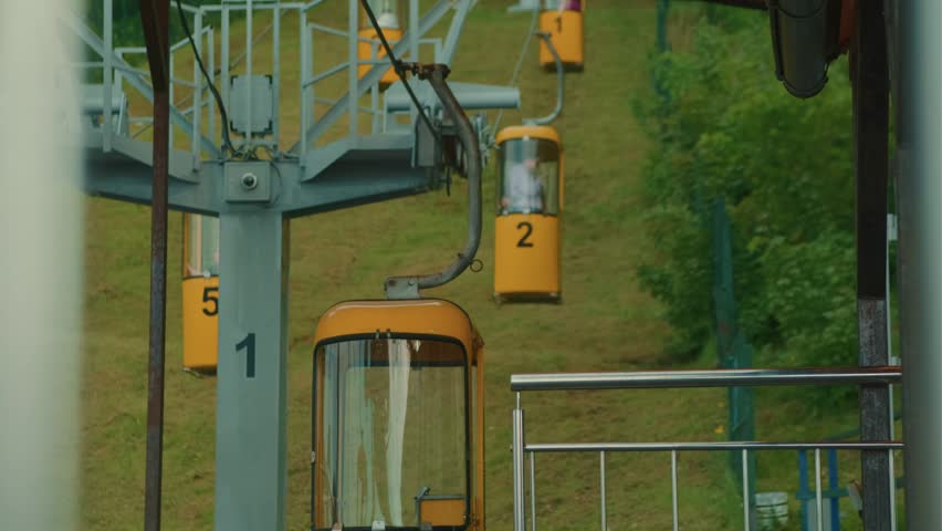 Yellow cable car moving in park. Tourists riding ropeway lift for sightseeing outdoor view. Transportation system over green hill for fun activity in summer day.