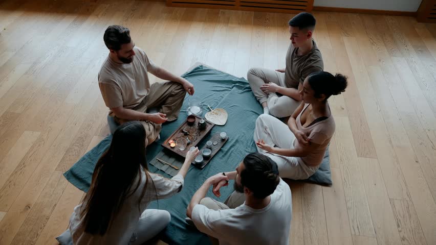 A group of four students and a male yoga mentor sit on cushions and talk