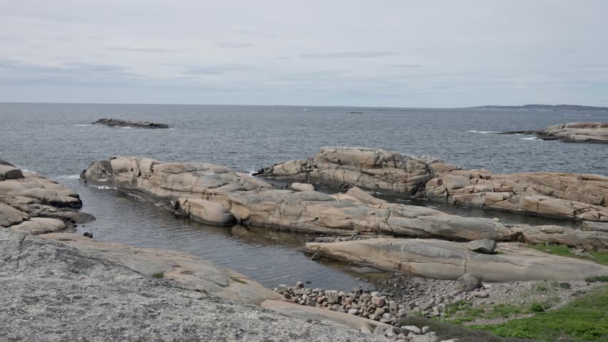 Large granite boulders forming a rugged shoreline with narrow water channels between them. Small pools of standing water and green vegetation in the foreground.