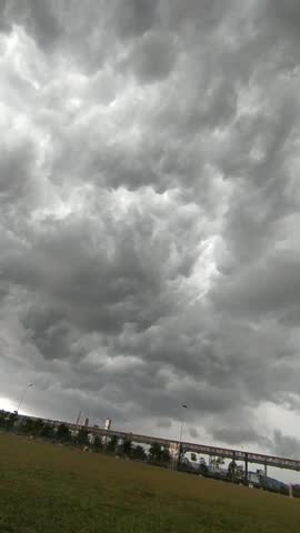 Dramatic storm clouds over green field and distant trees under overcast sky