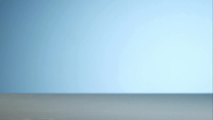 Multiple brass metal rifle and pistol bullets falling and bouncing on a white surface with a soft light blue studio gradient background in slow motion