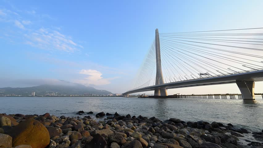 A scenic view of the modern Danjiang Bridge at sunset in Tamsui, New Taipei City, Taiwan, featuring the cable-stayed structure over the river.