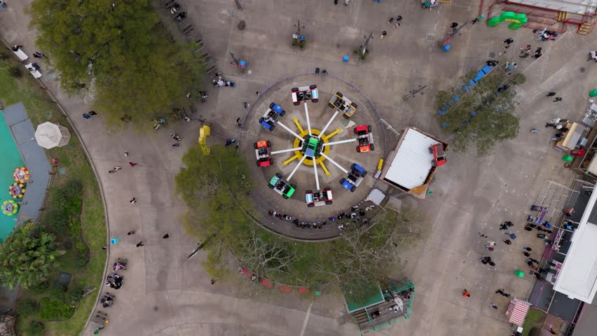 Aerial view of spinning amusement park ride with people nearby in urban plaza