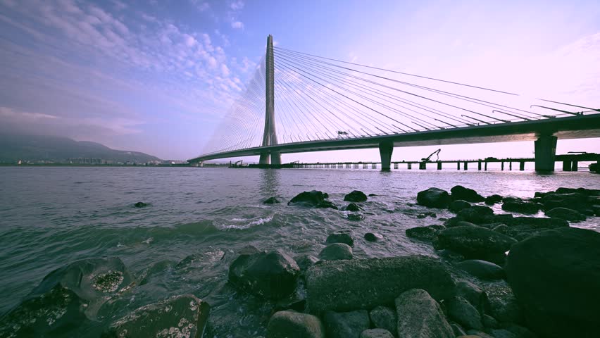 A scenic view of the modern Danjiang Bridge in Tamsui, New Taipei City, Taiwan, captured during a beautiful golden sunset over the river.