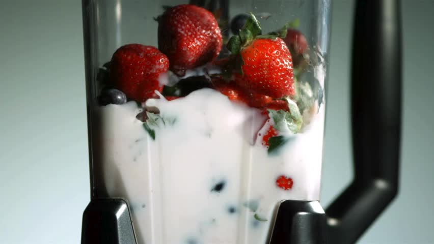 Fresh strawberries and blueberries being blended with white milk in a kitchen blender in slow motion creating a healthy and delicious fruit smoothie for breakfast