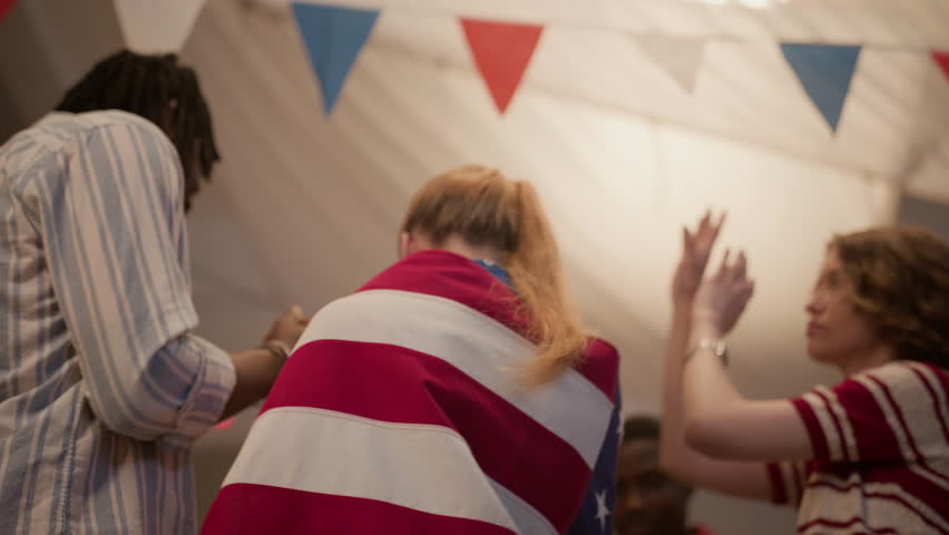Low angle shot of multiethnic young adults celebrating Independence Day, with Caucasian woman wrapped around USA flag. Footage is perfect for patriotic holiday marketing campaigns and ads
