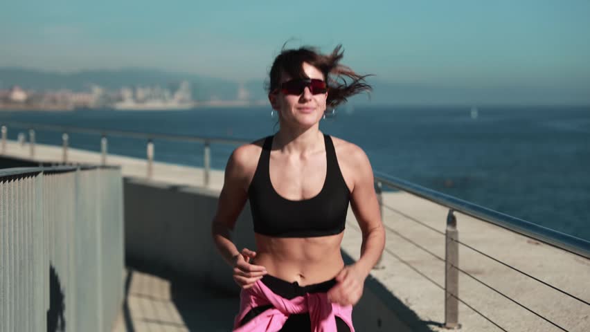 Young female runner stretching and exercising outdoors near a modern waterfront building.