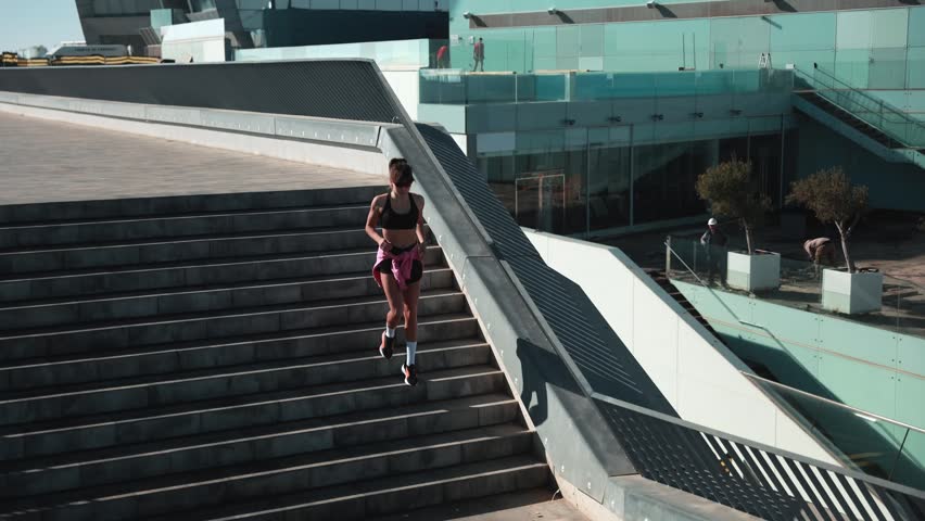 Young female runner stretching and exercising outdoors near a modern waterfront building.