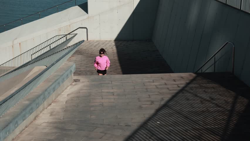 Young female runner stretching and exercising outdoors near a modern waterfront building.